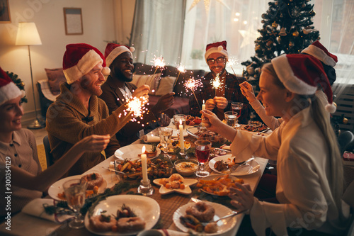 Multi-ethnic group of people holding sparklers while enjoying Christmas dinner at home photo