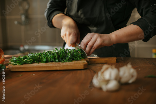 Closeup of female chef's hands preparing a recipe in the kitchen with vegetables. Woman cook chopping spinach leaves for vegetarian dish.
