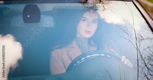 a young woman sitting in a car behind the wheel.she's going to go. in the glass of the car reflection of the sky. 4k proress 50p photo