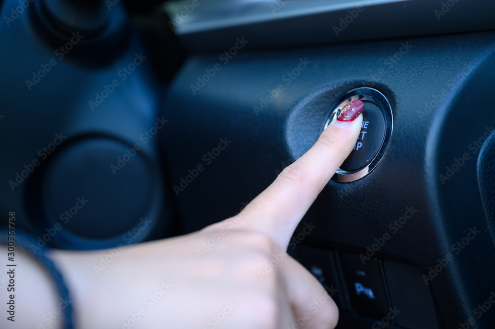 Close up female hand pressing engine push start button in modern car
