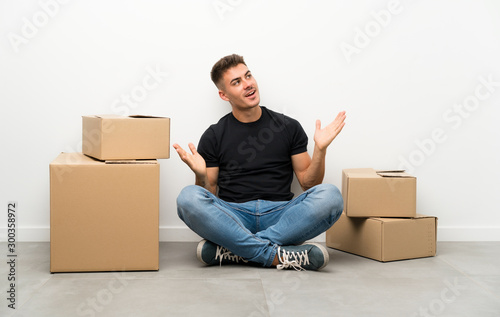 Handsome young man moving in new home among boxes with surprise facial expression