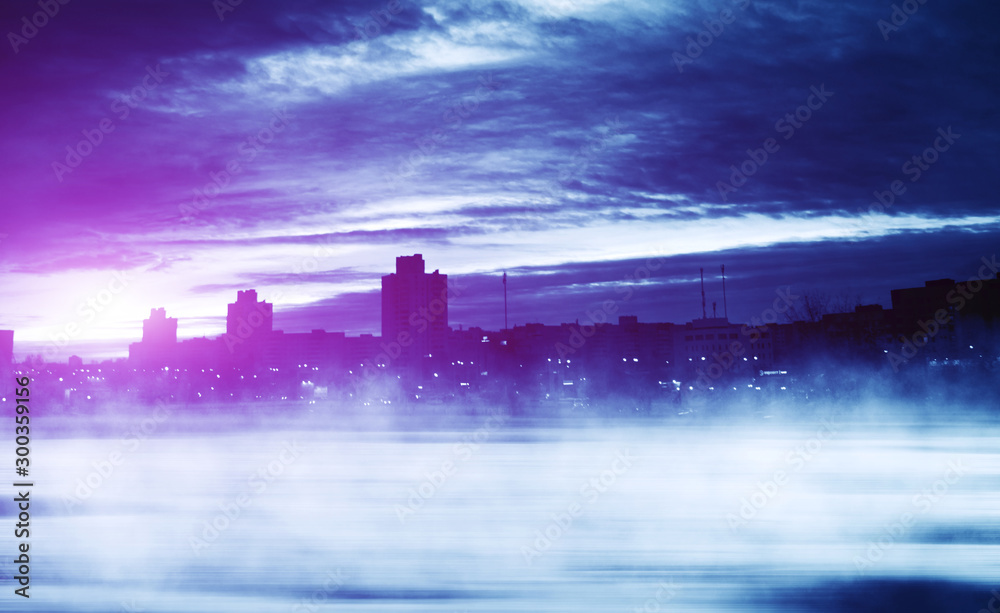 Fototapeta premium Background of winter night city. Snow covered road, fog. Reflections of the neon glow in the sky. Dawn over the winter city