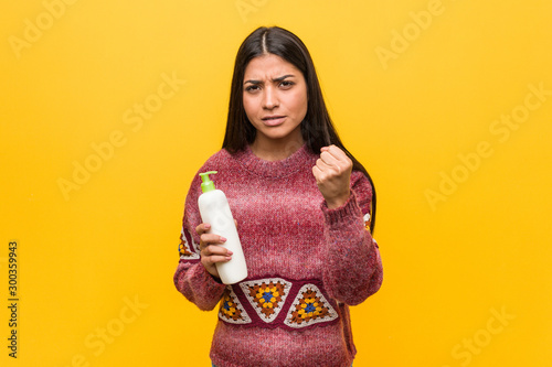 Young arab woman holding a cream bottle showing fist to camera, aggressive facial expression.