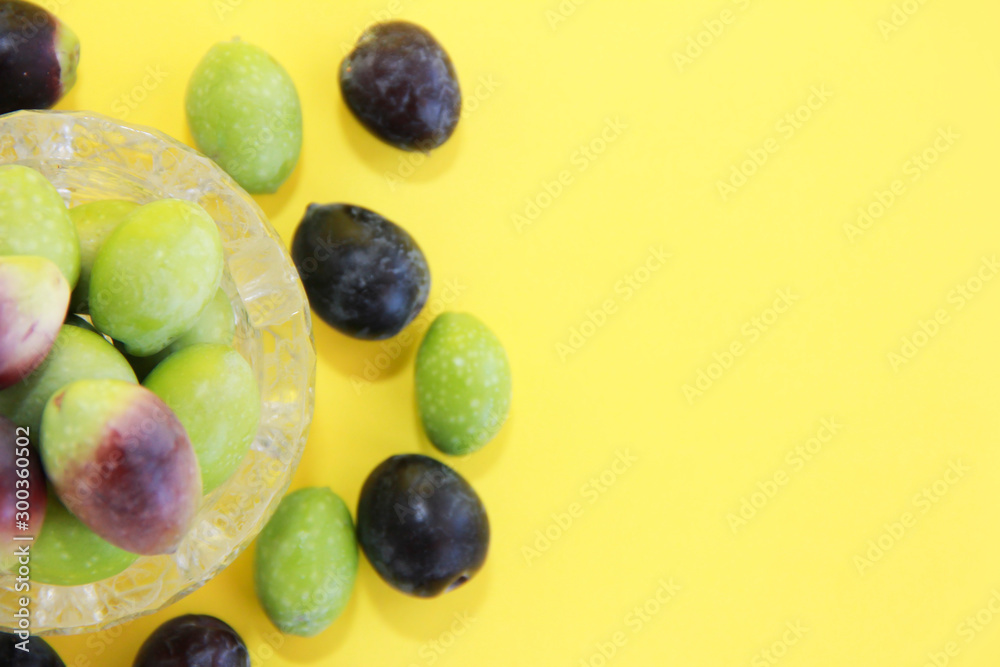 natural fresh round green and brown olives in a decorative glass plate on a yellow background natural fresh round green and brown olives in a decorative glass plate on a yellow background