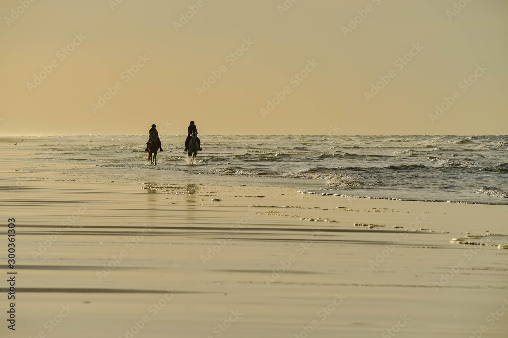 two horse riders on the beach under a beautiful sunset