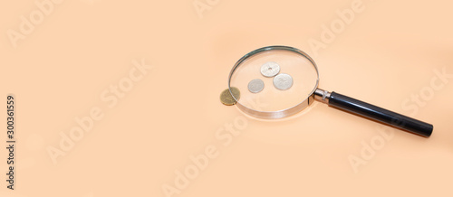Magnifier, coins on orange background.