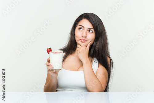 Young hispanic woman holding a smoothie young hispanic woman holding an avocado toast looking sideways with doubtful and skeptical expression.< mixto >