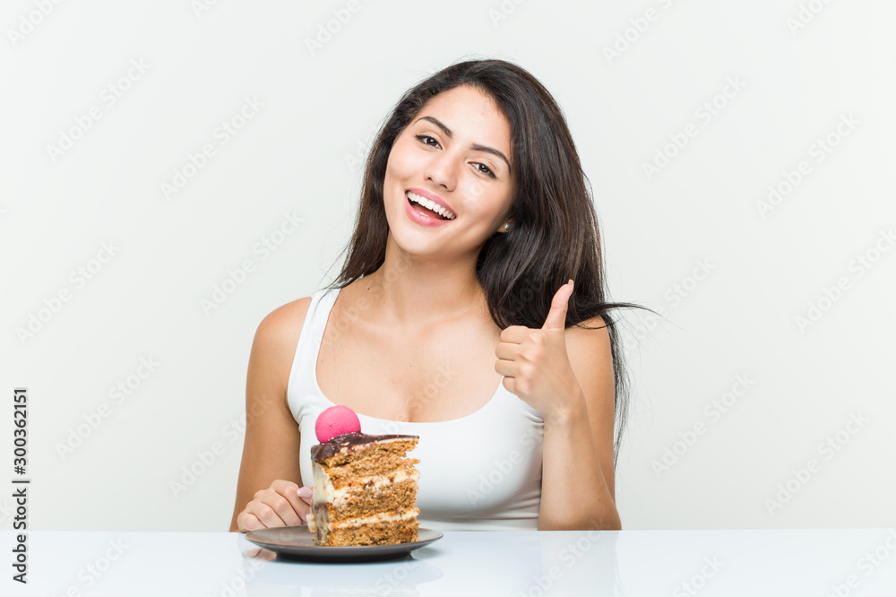 Young hispanic woman eating a cake smiling and raising thumb up Young hispanic woman eating a cake smiling and raising thumb up