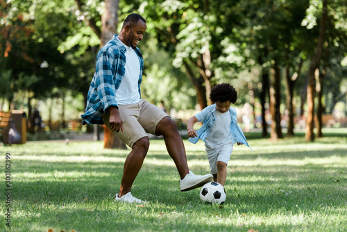 Fototapeta Naklejka Na Ścianę i Meble -  happy african american man playing football with curly son
