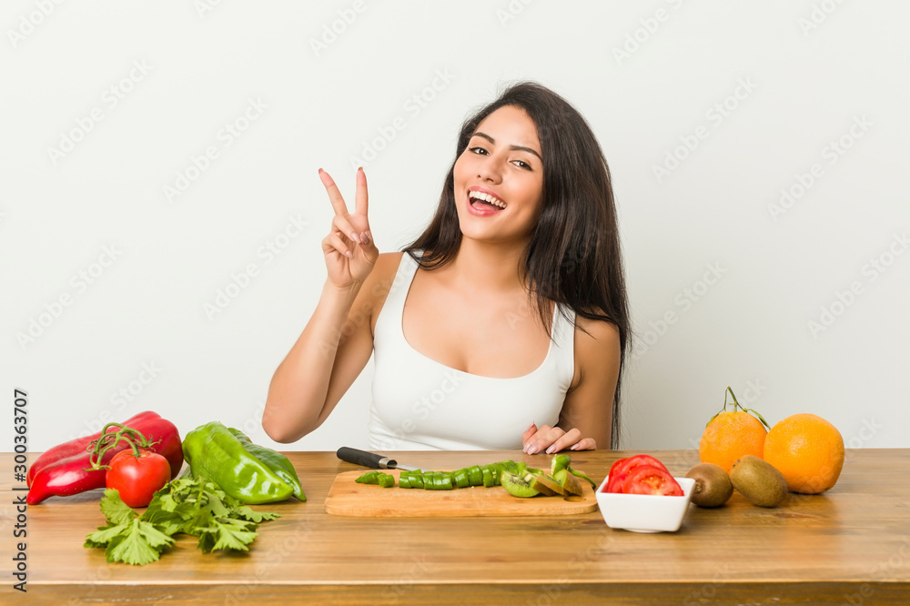 Young curvy woman preparing a healthy meal showing victory sign and smiling broadly. Young curvy woman preparing a healthy meal showing victory sign and smiling broadly.
