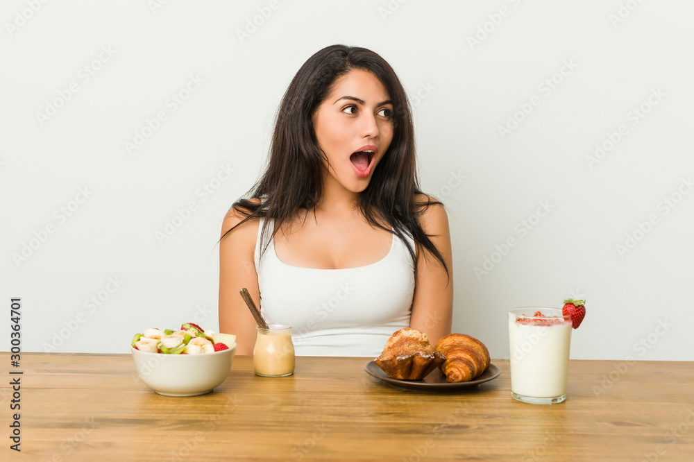 Young curvy woman taking a breakfast being shocked because of something she has seen.