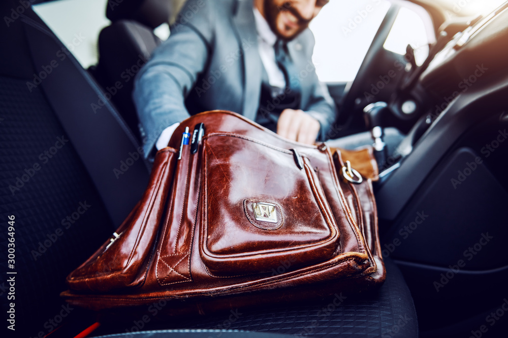 Businessman sitting in his car and taking out something from his briefcase. Selective focus on briefcase. - obrazy, fototapety, plakaty 