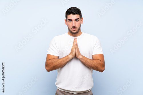 Caucasian handsome man over isolated blue background keeps palm together. Person asks for something