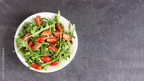 Salad with fresh green arugula and tomato cherry in a white ceramic bowl.