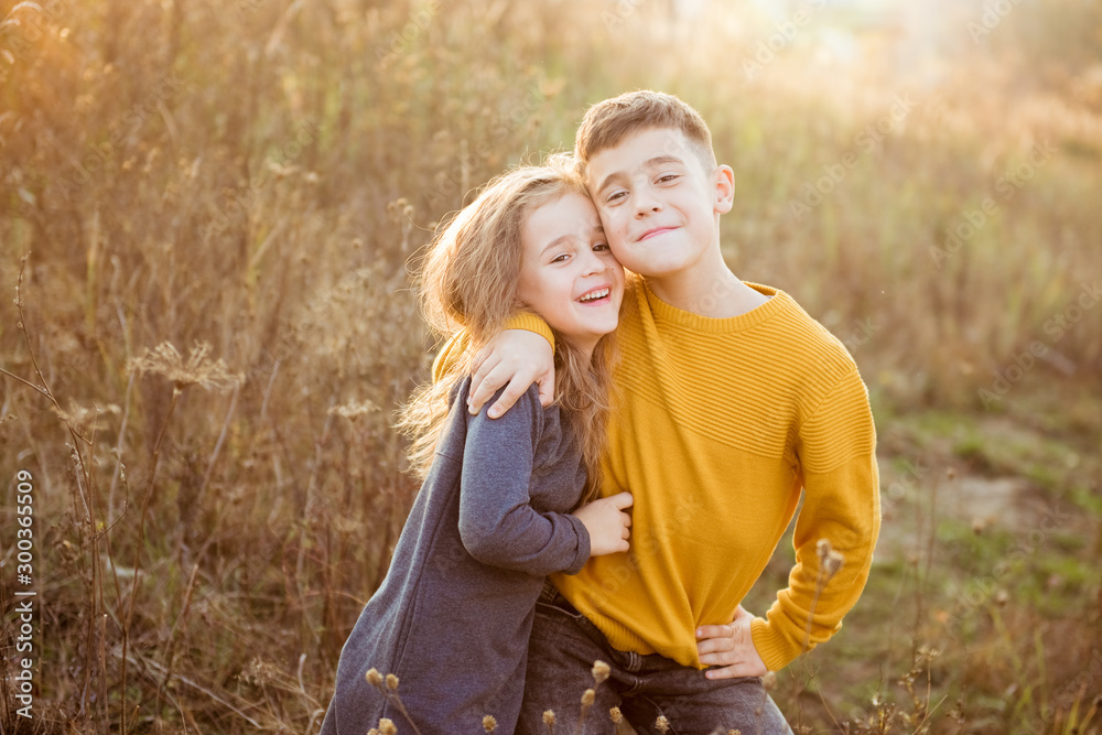 Fototapeta premium Little pretty girl and young boy hugging each other on autumn day. Brother and little sister cuddling. Happy family