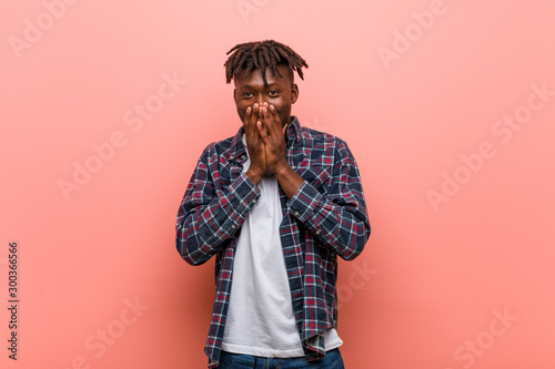 Young african black man laughing about something, covering mouth with hands.
