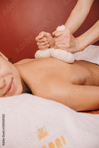 cropped view of masseur doing back massage with herbal balls to woman in spa