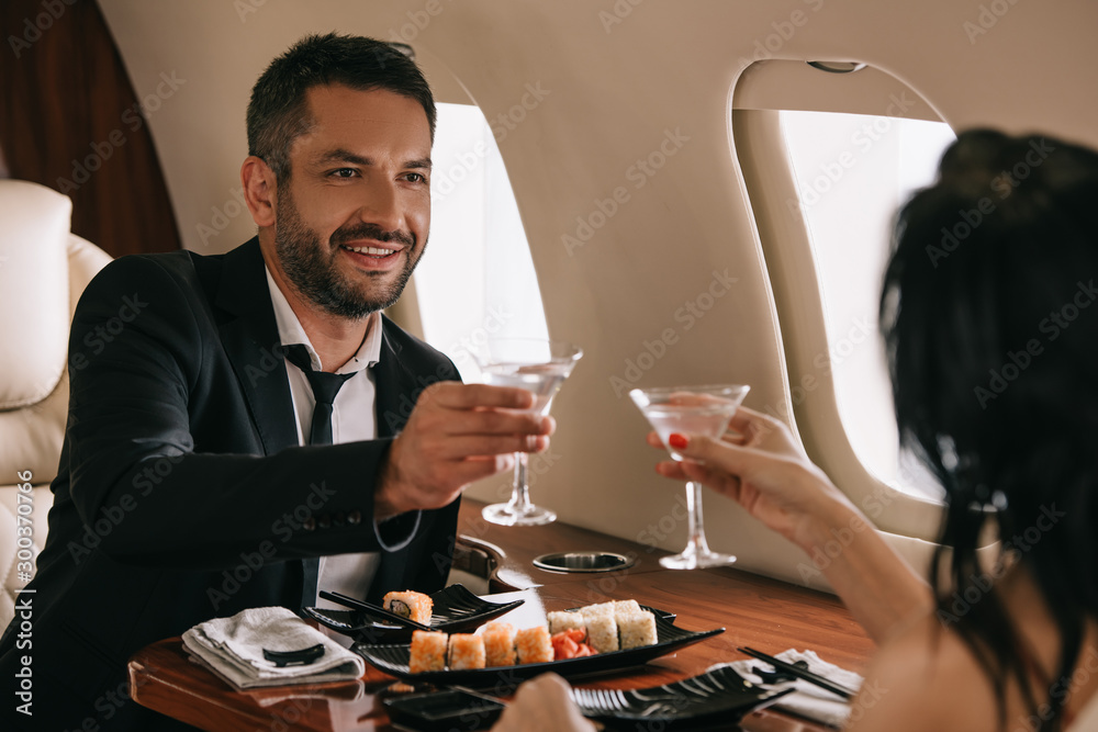 cropped view of woman holding martini glasses near happy man in private jet cropped view of woman holding martini glasses near happy man in private jet