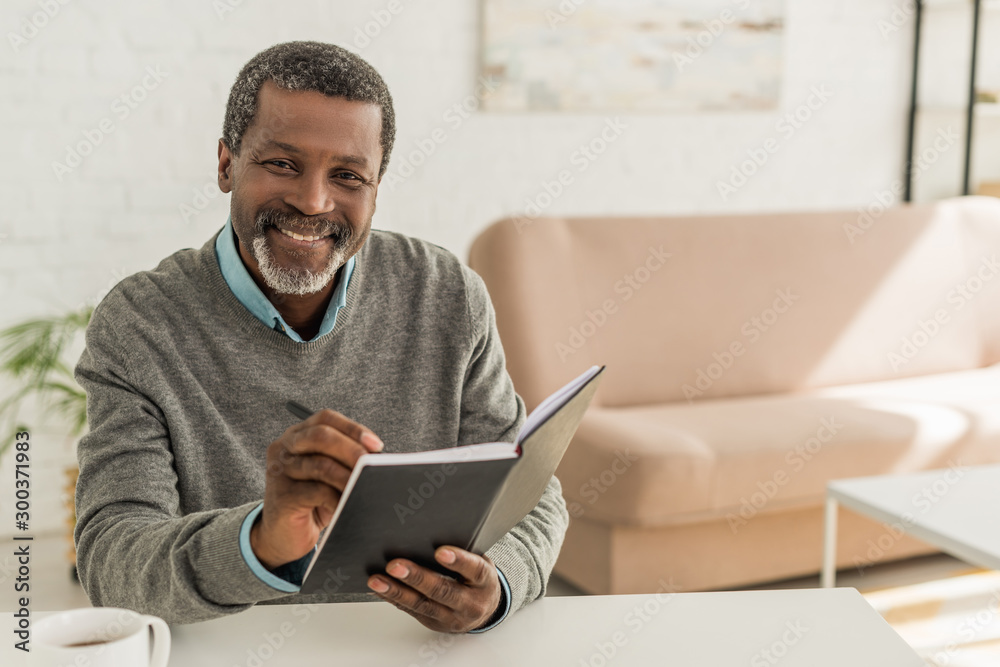 cheerful african american man smiling at camera while holding notebook cheerful african american man smiling at camera while holding notebook