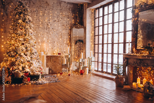 warm cozy evening luxury Christmas room interior design, Xmas tree decorated by gold lights presents gifts, candles,mirror garland lighting fireplace.holiday living room. New year holidays concept