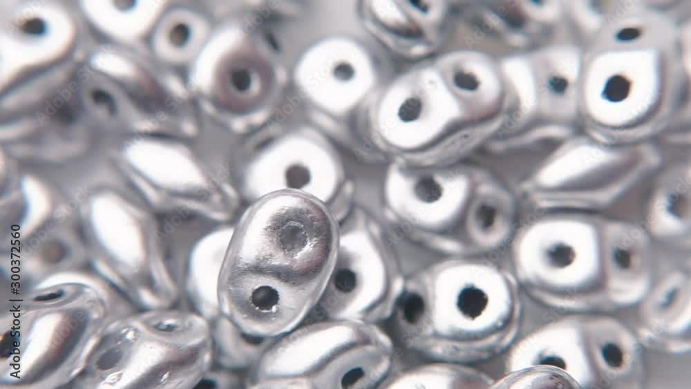 A macro shot of pouring silver beads with two holes. A macro shot of pouring silver beads with two holes.