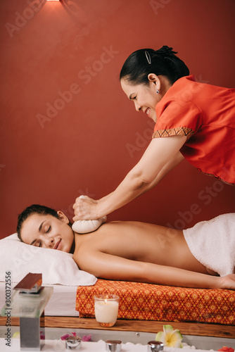 side view of asian masseur doing back massage with herbal balls to woman in spa