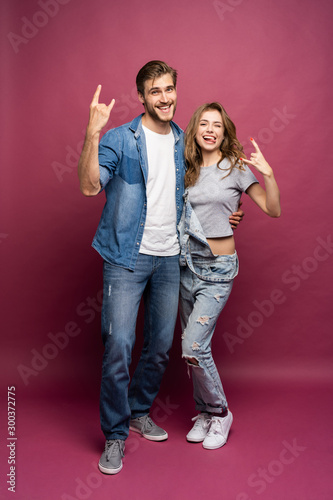 smiling young casual couple making victory or peace sign on pink background.