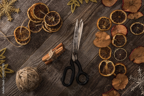 top view of dried citrus and apple slices near snowflakes, scissors, thread and cinnamon on wooden surface