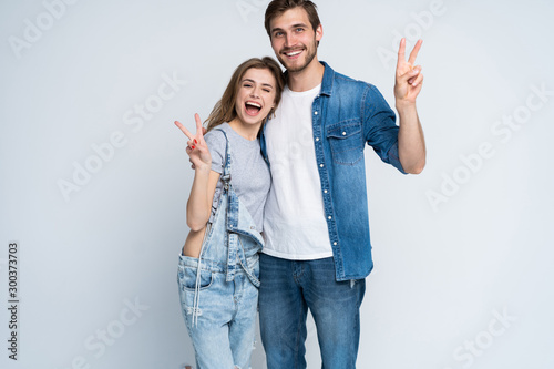 smiling young casual couple making victory or peace sign on white background.