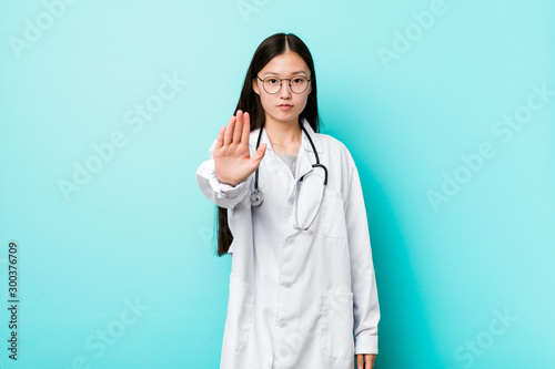 Young chinese doctor woman standing with outstretched hand showing stop sign  preventing you.