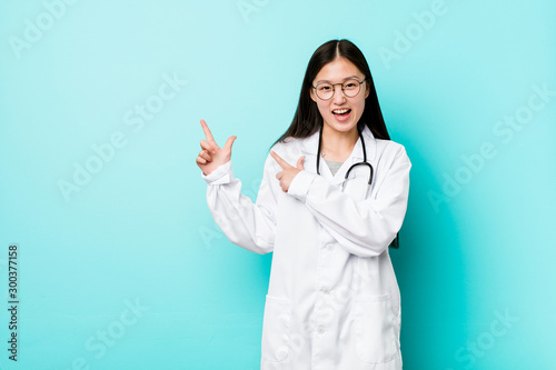 Young chinese doctor woman pointing with forefingers to a copy space  expressing excitement and desire.