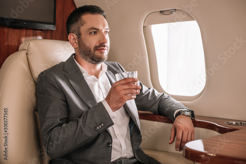 selective focus of handsome bearded businessman holding glass while sitting in private jet © LIGHTFIELD STUDIOS