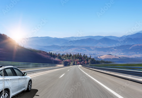 White car moves on the road among the mountains and forests.