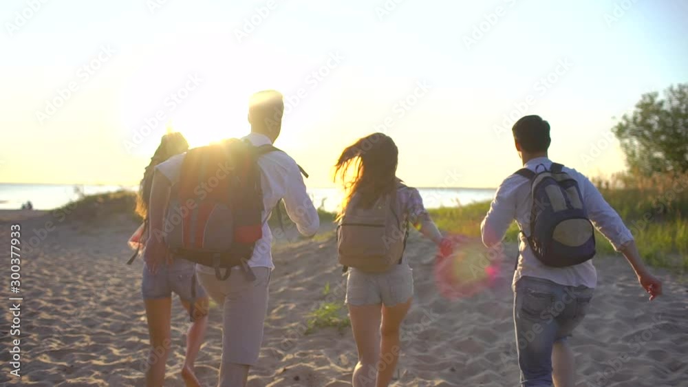 Group of young hikers tourists running jumping at beach nature at sunset. Hipster friends woman man travelers hiking with backpack, summer trip vacation adventure travel tourizm landscape ocean slowmo