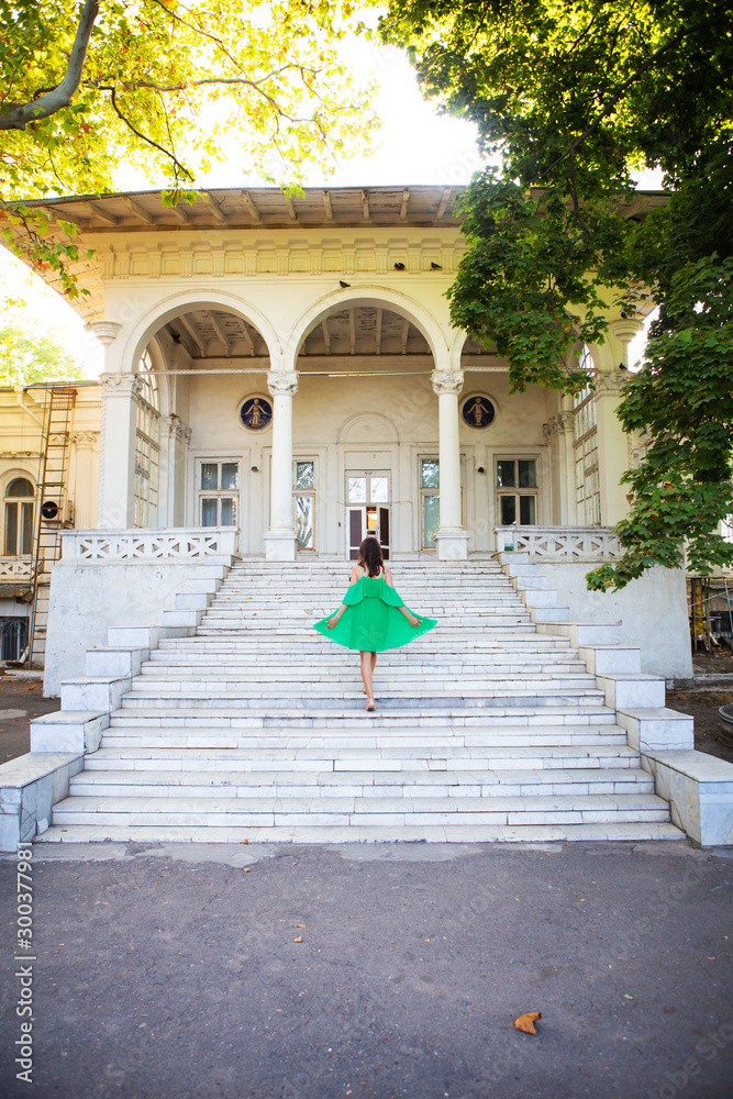 Summer vacation. A girl in a green dress stands on the stairs near the sanatorium. Chkalov in Odessa. - obrazy, fototapety, plakaty 
