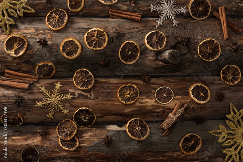 top view of dried citrus slices with anise, cinnamon sticks and decorative snowflakes on wooden background