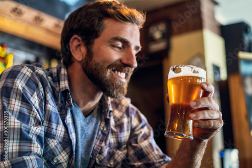 Smiling man looking at beer glass in the bar photo