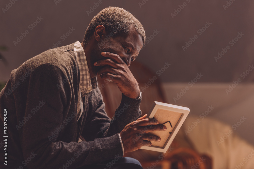 senior, depressed african american man looking at photo frame - obrazy, fototapety, plakaty 