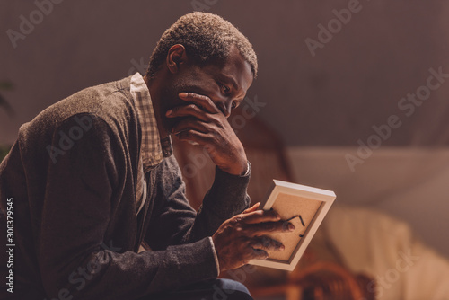 senior, depressed african american man looking at photo frame