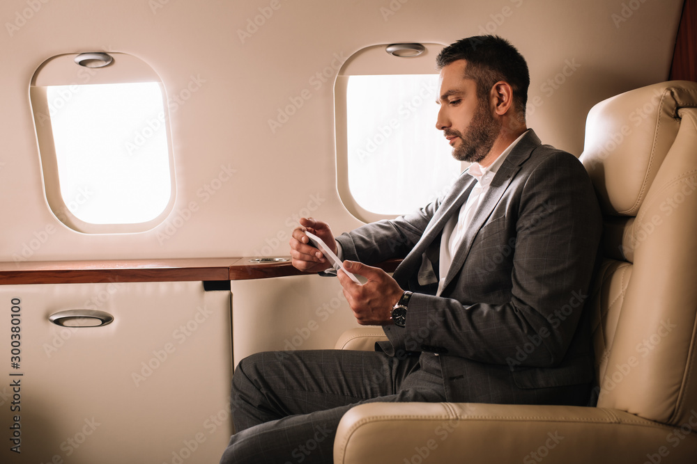 side view of handsome businessman in suit using smartphone in private jet side view of handsome businessman in suit using smartphone in private jet