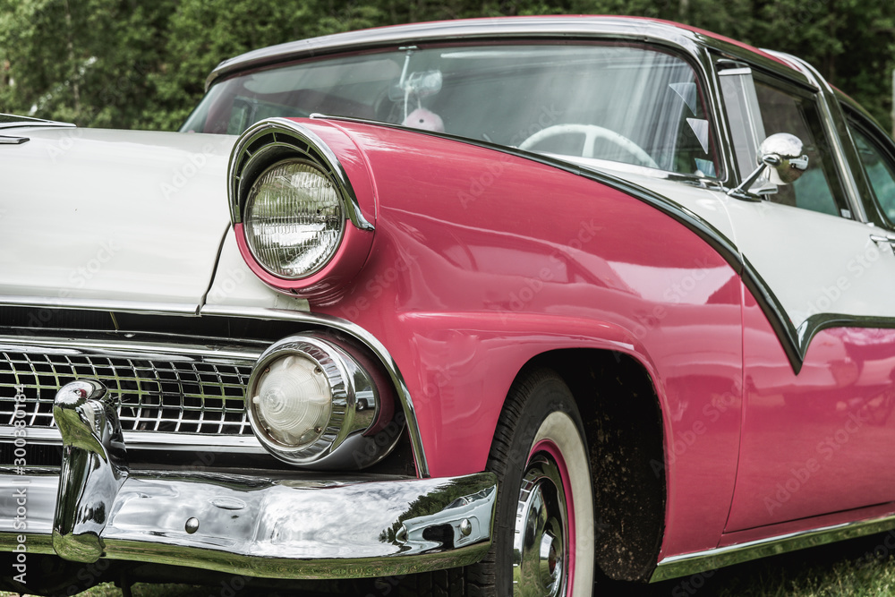 Partial front view of pink and white classic car from the fifties