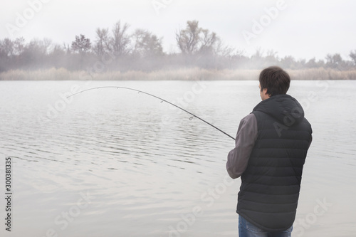 Fisher man fishing with spinning rod on a river bank at misty foggy sunrise © eliosdnepr