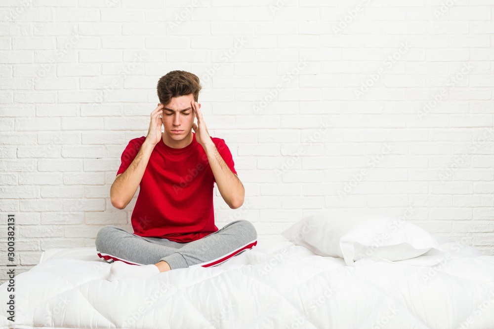 Obraz premium Young teenager student man on the bed touching temples and having headache.