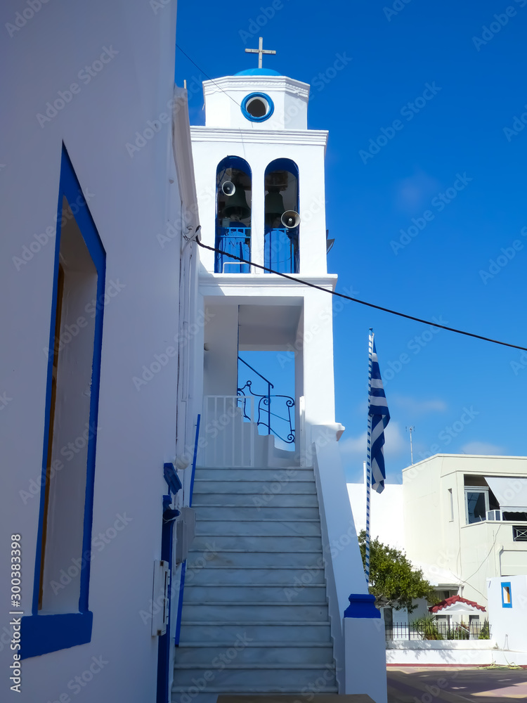 Stepped front of a white and blue Orthodox church with bell tower and Greek flag