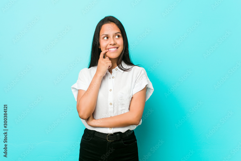 Young hispanic cool woman against a blue wall relaxed thinking about something looking at a copy space. Young hispanic cool woman against a blue wall relaxed thinking about something looking at a copy space.