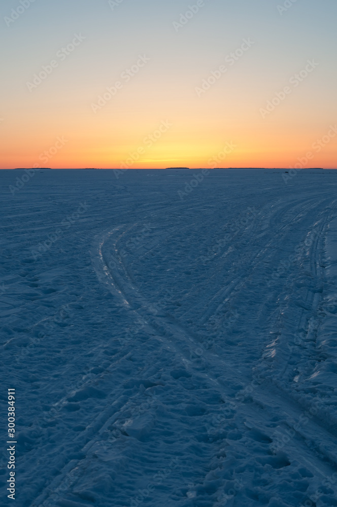 Frozen ski tracks on sea-ice with the setting sun coloring the sky with orange and pink in Pori, Finland
