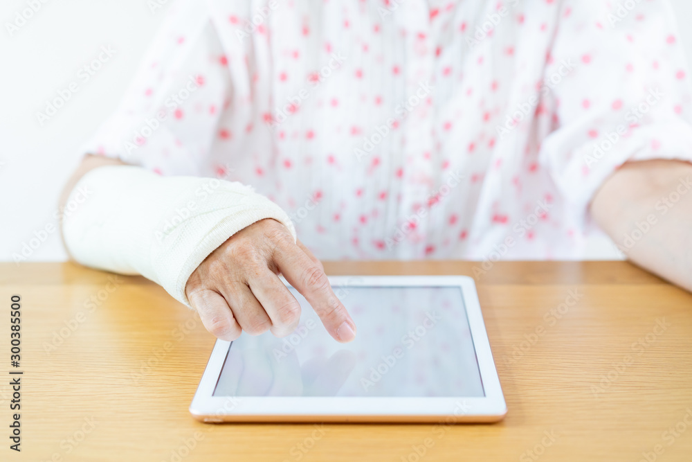 Injured arm woman reading an e-book on the tablet close up. Healthcare and wellness in aging society concept. Injured arm woman reading an e-book on the tablet close up. Healthcare and wellness in aging society concept.