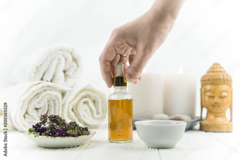 Spa treatment bottle of natural organic oil essence serum collagen. Towel, aromatic candles, flowers, massage brush and Buddha on white background. Copy space for text. Beautiful woman hands. Oil drop Spa treatment bottle of natural organic oil essence serum collagen. Towel, aromatic candles, flowers, massage brush and Buddha on white background. Copy space for text. Beautiful woman hands. Oil drop
