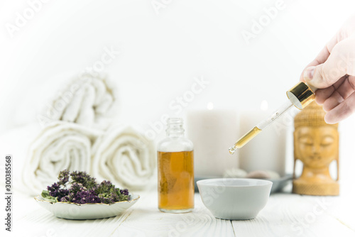 Spa treatment bottle of natural organic oil essence serum collagen. Towel  aromatic candles  flowers  massage brush and Buddha on white background. Copy space for text. Beautiful woman hands. Oil drop
