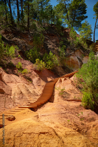 View over the ochre steps and stairway between orange rocks, yellow sand and pinetrees in Roussillion, Vaucluse-Luberon, France in the summer.
